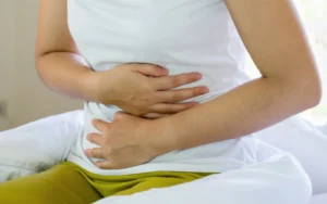 Woman in a white shirt holding her stomach while sitting