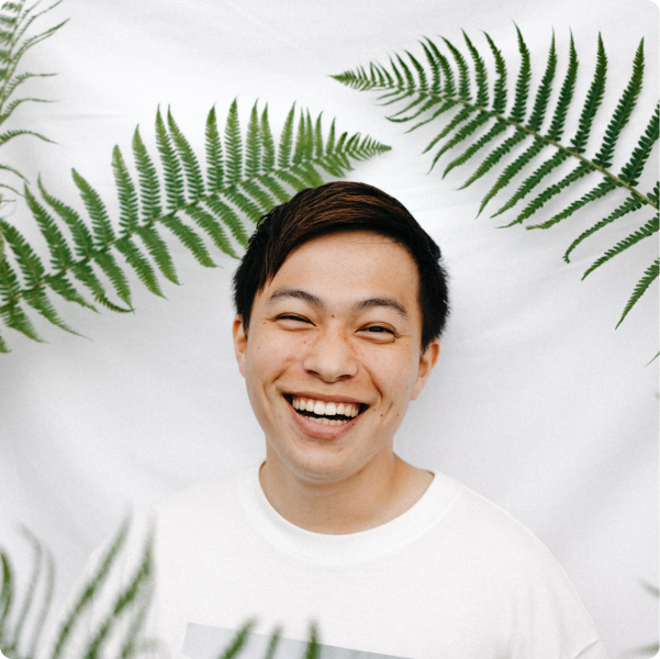 A young man smiling next to green plant leaves