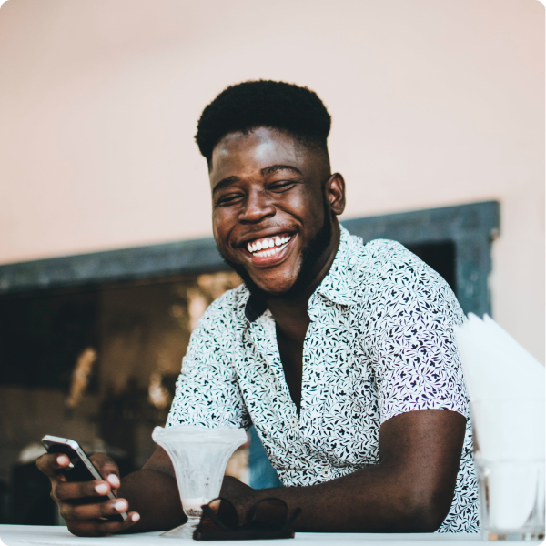 Young man smiling while holding his phone and having coffee